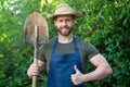 Happy gardener man in gardening apron and farmers hat with garden spade giving thumb gesture Royalty Free Stock Photo