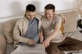 Happy gay couple with casual clothes spending time together at home and watching movie on the laptop. Two caucasian men Royalty Free Stock Photo