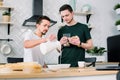 Happy gay couple preparing breakfast in kitchen at morning. Handsome man putting breakfast cereals in white bowls, while