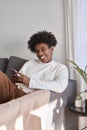 Happy gen z African American teen sitting on couch using mobile phone. Royalty Free Stock Photo