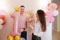 Happy and gentle parents hold baby daughter with birthday balloon decor. Royalty Free Stock Photo