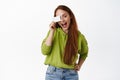 Happy ginger girl shows her credit card, paying for purchase contactless, going shopping, standing against white