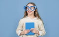 Happy girl back to school with book wearing big funny heart-shaped glasses blue background Royalty Free Stock Photo