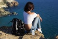 Happy girl backpacker is sitting on rock peak over sea
