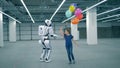 Happy girl with balloons is running around an anthropoid robot