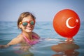 Happy girl bathes in sea water. Vacation in Turkey. Turkish flag on balloon. Smiling girl on sea.