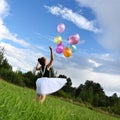 happy girl beautiful dress is holding colorful balloons in summer meadow against background of blue sky and clouds Royalty Free Stock Photo