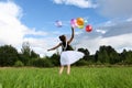 happy girl in beautiful dress holds colorful balloons in summer meadow against background of blue sky and clouds Royalty Free Stock Photo