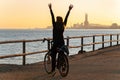 Happy girl with a bicycle raised her hands up and enjoys the sunset on the promenade road of Maresme, Catalonia, Spain Royalty Free Stock Photo