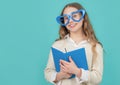 Happy girl in big funny heart-shaped glasses holding school book blue background Royalty Free Stock Photo