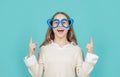 Happy girl in big funny heart-shaped glasses pointing fingers up blue background, copy space Royalty Free Stock Photo