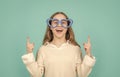 Happy girl in big funny heart-shaped glasses pointing fingers up blue background, copy space Royalty Free Stock Photo