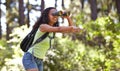 Happy girl, binoculars and pointing in nature with backpack for sightseeing, explore or outdoor vision. Young female