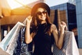 Happy girl, in a black dress and hat, wearing dark glasses, holding shopping bags and enjoying shopping, Black Friday Royalty Free Stock Photo