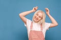 Happy girl blond girl listens to music in headphones with eyes closed on a blue background, dancing and smiling. Smiling teen girl Royalty Free Stock Photo