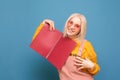 Happy girl blonde in bright clothes and pink glasses poses with a broom in her hands on a blue background, looks at the camera and Royalty Free Stock Photo