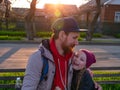 Happy girl with braided hair and father in spring park sits on a bench on sunset outdoor.Kid with dad smiling having fun