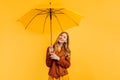 Happy girl, in a bright yellow dress and an autumn jacket, stands with a yellow umbrella on an  yellow background. Autumn Royalty Free Stock Photo