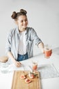 Happy girl with buns smiling stretching glass with grapefruit detox smoothie to somebody. White wall background. Healthy