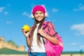 Happy girl in casual fashion style listen to music in modern headphones holding apple fruit for travel sunny outdoors