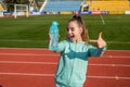Happy girl child in activewear stand at sports stadium pointing finger at sport water bottle, hydration Royalty Free Stock Photo
