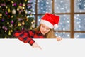 Happy girl in christmas hat peeking and pointing down at empty board. Space for text Royalty Free Stock Photo