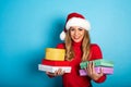 Happy girl with Christmas hat receives a lot of presents. Cyan background Royalty Free Stock Photo