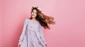 Happy girl in circlet of flowers posing with hair waving. Indoor photo of caucasian smiling lady playing with her purple