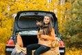 Happy girl and dog sitting in the trunk of a car in nature. Friendship of a man and a dog, travel, camping on an autumn background Royalty Free Stock Photo