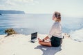 Woman sea laptop yoga. Business woman freelancer in yoga pose working over blue sea beach at laptop and meditates. Girl Royalty Free Stock Photo