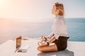 Woman sea laptop yoga. Business woman freelancer in yoga pose working over blue sea beach at laptop and meditates. Girl Royalty Free Stock Photo