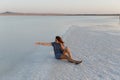 Happy girl enjoying the sunset, touches water of a salt lake sitting on crystals