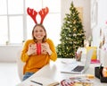 Happy girl freelancer laughs and hugs holiday gift at home office before Christmas