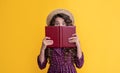 happy girl with frizz hair hiding behind book on yellow background