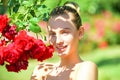 Happy girl in a garden with red roses. Beautiful young woman smelling a rose flower. Royalty Free Stock Photo