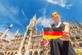 Happy girl with a German flag poses against the background of the city hall in Munich. Travel and immigration to Germany Royalty Free Stock Photo