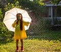 A happy girl jumps with a green umbrella in the summer rain. The girl is dressed in a yellow raincoat and enjoys the Royalty Free Stock Photo