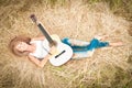 Happy girl with guitar lying on grass in meadow.