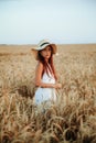 Happy girl in a hat stands in a field of ripe wheat in the sunset light. Sunset sun. Walking in the wheat field Royalty Free Stock Photo