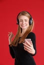 Happy girl with headphones, smiling and holding mobile phone on outstretched hand. On a red background. Royalty Free Stock Photo