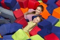 Happy girl and her mom lying among soft cubes in pit at amusement center
