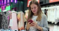 Happy girl holding bags with purchases, smiling while looking at phone in shopping center. Received good news, reading