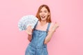 Happy girl holding cash dollar bills and showing a winning gesture on an isolated pink background Royalty Free Stock Photo