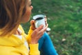 Happy girl holding in hands cup of hot tea on green grass in outdoors nature park, beautiful woman hipster enjoy drinking cup Royalty Free Stock Photo