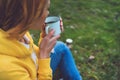 Happy girl holding in hands cup of hot tea on green grass in outdoors nature park, beautiful woman hipster enjoy drinking cup Royalty Free Stock Photo