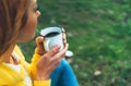 Happy girl holding in hands cup of hot tea on green grass in outdoors nature park, beautiful woman hipster enjoy drinking cup Royalty Free Stock Photo