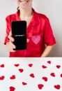 A happy girl is holding a smartphone with an activated screen with 1 SMS message in the shape of a heart. Concept of Valentine`s