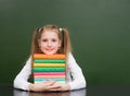 Happy girl hugs pile books near empty green chalkboard Royalty Free Stock Photo