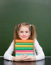 Happy girl hugs pile books near empty green chalkboard Royalty Free Stock Photo