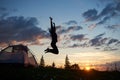 Happy girl jumping on grass with wildflowers at camping in mountains at dawn under blue sky Royalty Free Stock Photo